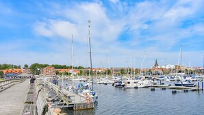 Uma marina com barcos atracados, um cais de madeira e edifícios ao fundo.