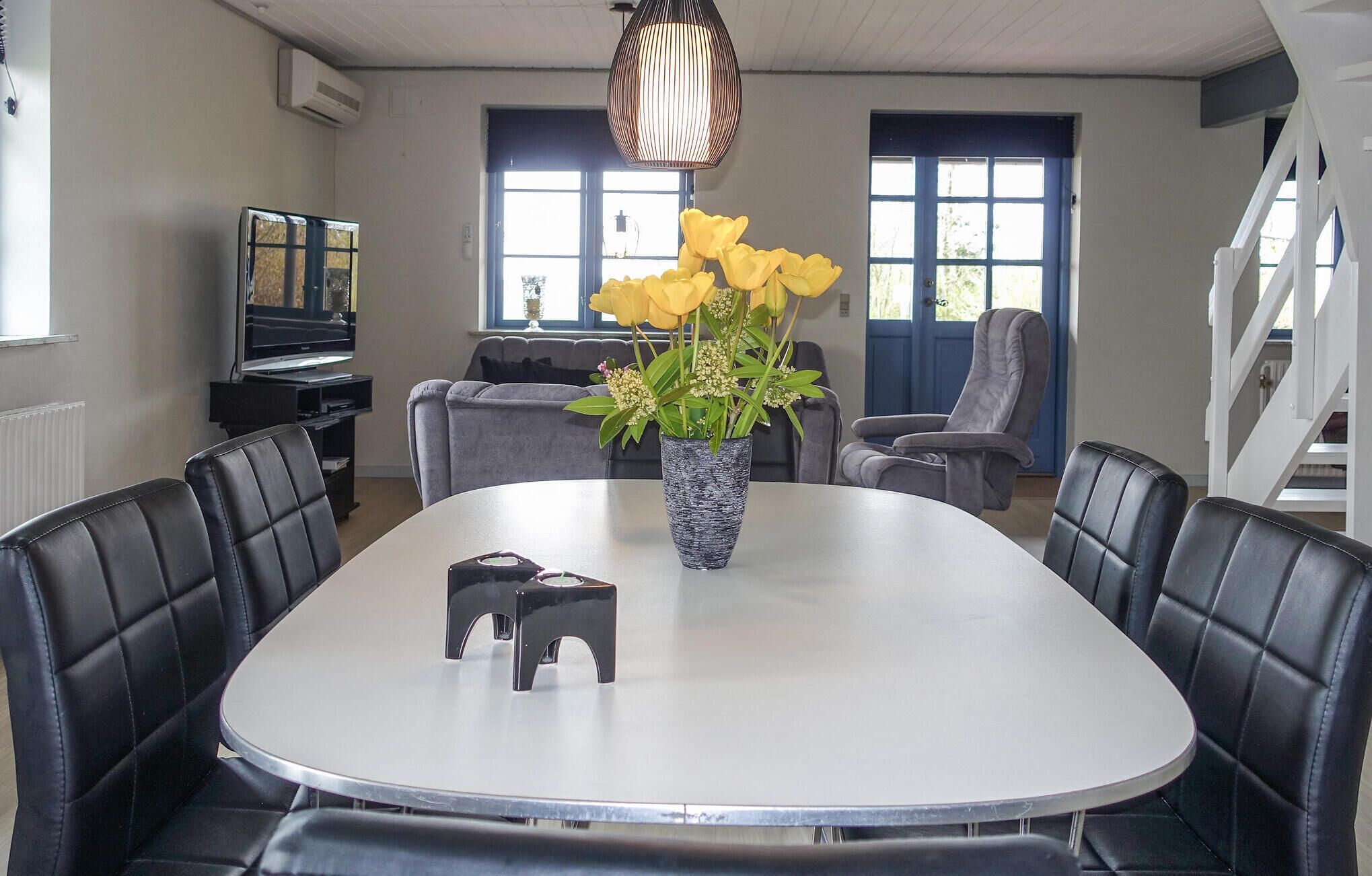 Un coin repas avec une table ronde, des chaises en cuir noir, un vase rempli de fleurs jaunes et un luminaire suspendu.