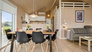 A modern kitchen with wooden cabinets, a dining table with chairs, and a sofa in a living area with a large window. - 2 bedroom gorgeous home in Haarby (Haarby)