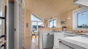 A modern kitchen with wooden paneling, a dishwasher, and a window overlooking a residential area. - 2 bedroom gorgeous home in Haarby (Haarby)