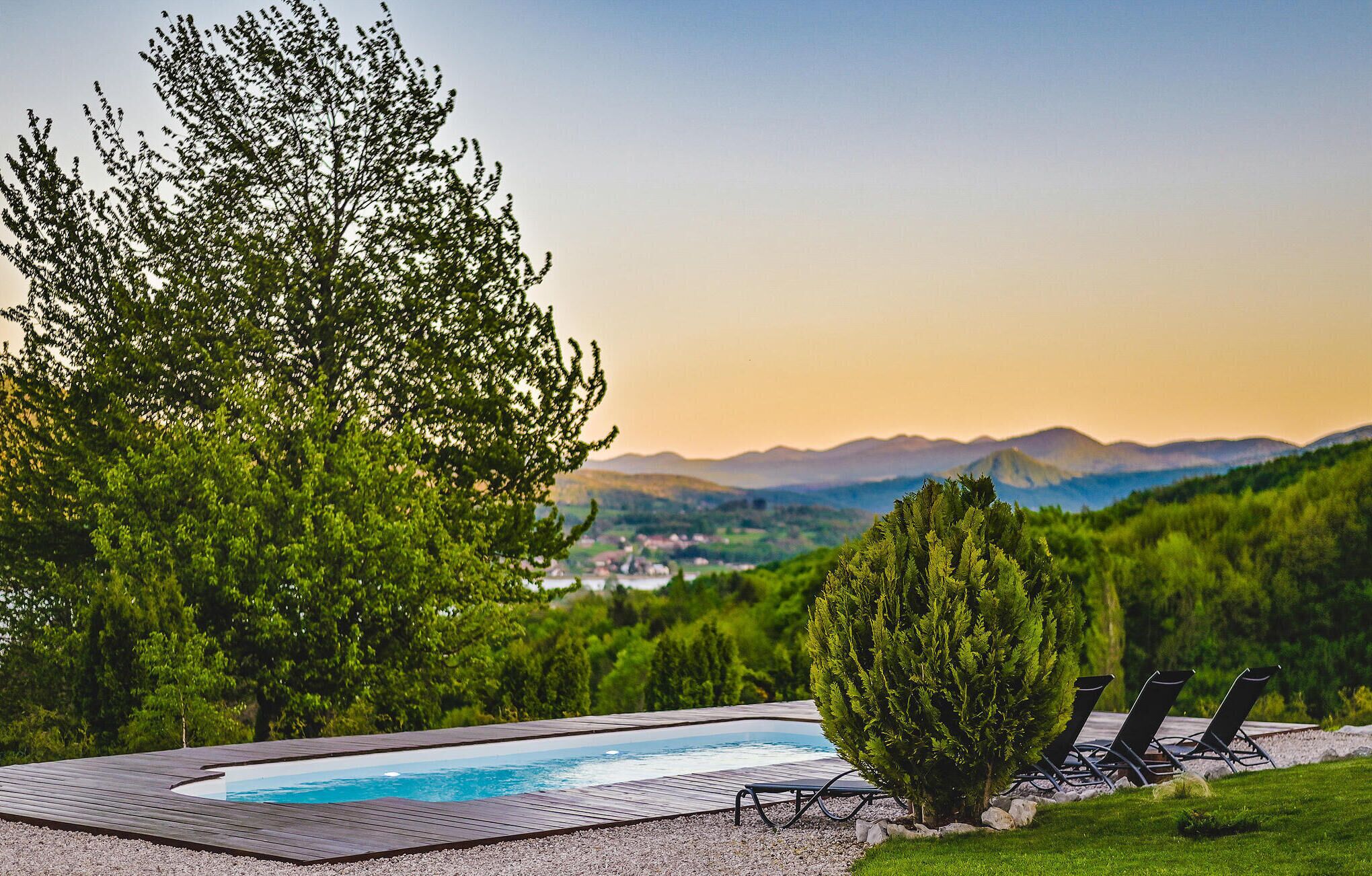A swimming pool with a wooden deck, surrounded by trees and a view of mountains.