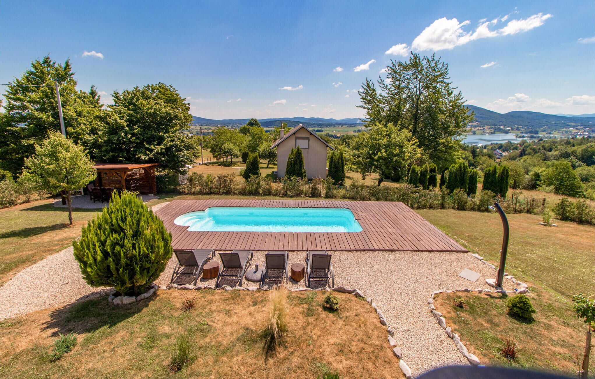 Piscina rectangular con muelle de madera, rodeada por una zona de grava con sillas de descanso y un cobertizo pequeño.