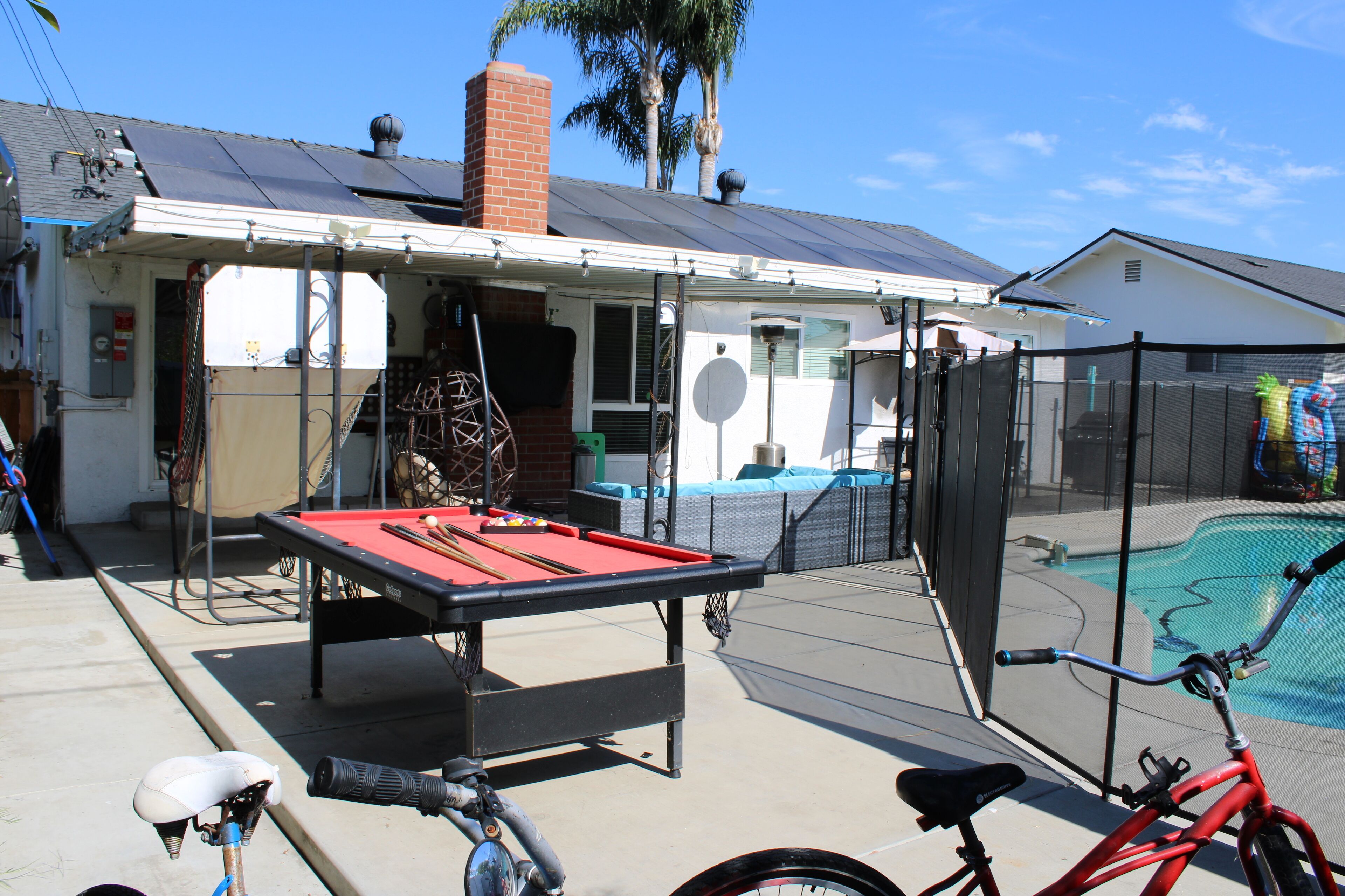 Una mesa de billar en un patio trasero, con una bicicleta y una piscina.
