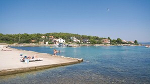 Une zone côtière avec des eaux cristallines, une plage de sable et des bâtiments visibles à l’arrière-plan.