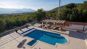 Un espace piscine agrémenté d’une pergola, de chaises longues et offrant une vue sur un paysage montagneux.