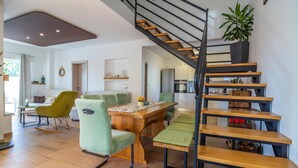 Un espace de vie moderne avec un escalier en bois, un coin repas avec des chaises vertes et une cuisine visible au fond.