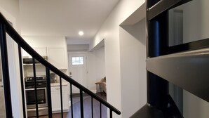 En trappe fører op til et køkken med hvide skabe og en indbygget ovn.