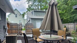 En udendørs terrasse med et rundt bord, fire stole og en stor parasol.