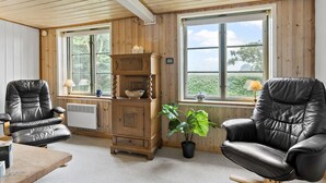 A cozy room with wooden walls and ceiling, two leather chairs, a wooden cabinet, and a large window with a view of greenery. - Beautiful home in Aakirkeby with WiFi (Aakirkeby)