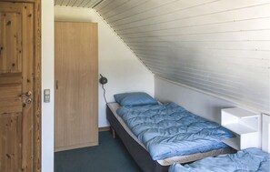 Una habitación pequeña con cama individual, techo inclinado, puerta de madera y mesita de noche.