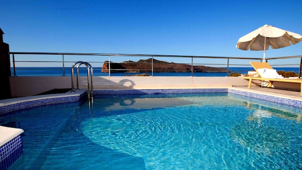 Ein Schwimmbecken mit klarem, blauem Wasser, einer Metallleiter und Blick auf das Meer und einen entfernten Berg.