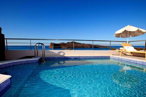 A swimming pool with clear blue water, a metal ladder, and a view of the sea and a distant mountain.