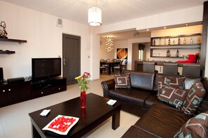 A modern living room with a dark brown sofa, a coffee table with a vase of flowers, and a flat-screen TV.