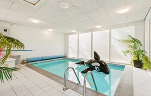 An indoor swimming pool with a dolphin sculpture, tiled walls, and potted plants. - 4 bedroom nice home in Nexø (Nexø)