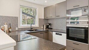 A modern kitchen with a built-in dishwasher, a coffee maker, and a window overlooking a wooded area. - 4 bedroom nice home in Nexø (Nexø)