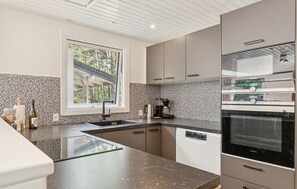 Una cucina moderna con lavastoviglie integrata, una macchina del caffè e una finestra con vista su una zona boschiva.