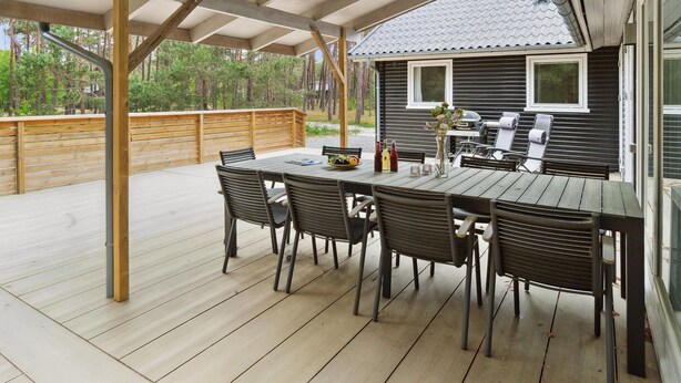 An outdoor patio with a wooden table and chairs, a grill, and a view of a house with a tiled roof. - 4 bedroom nice home in Nexø (Nexø)