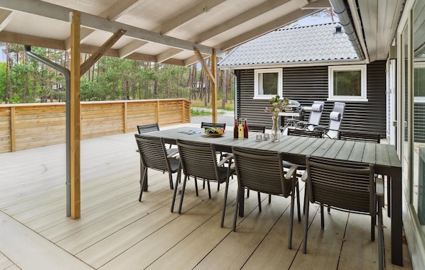 An outdoor patio with a wooden table and chairs, a grill, and a view of a house with a tiled roof.