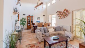 A cozy living room with a sectional sofa, a coffee table, a bookshelf, and a dining area with wicker chairs. - Beach front home in Mallorca (Mallorca)