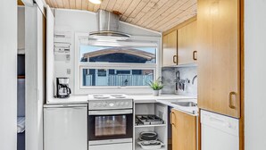 Cocina compacta con estufa, horno y cafetera. Incluye un ventanal con vista a una cerca azul y un techo de madera.