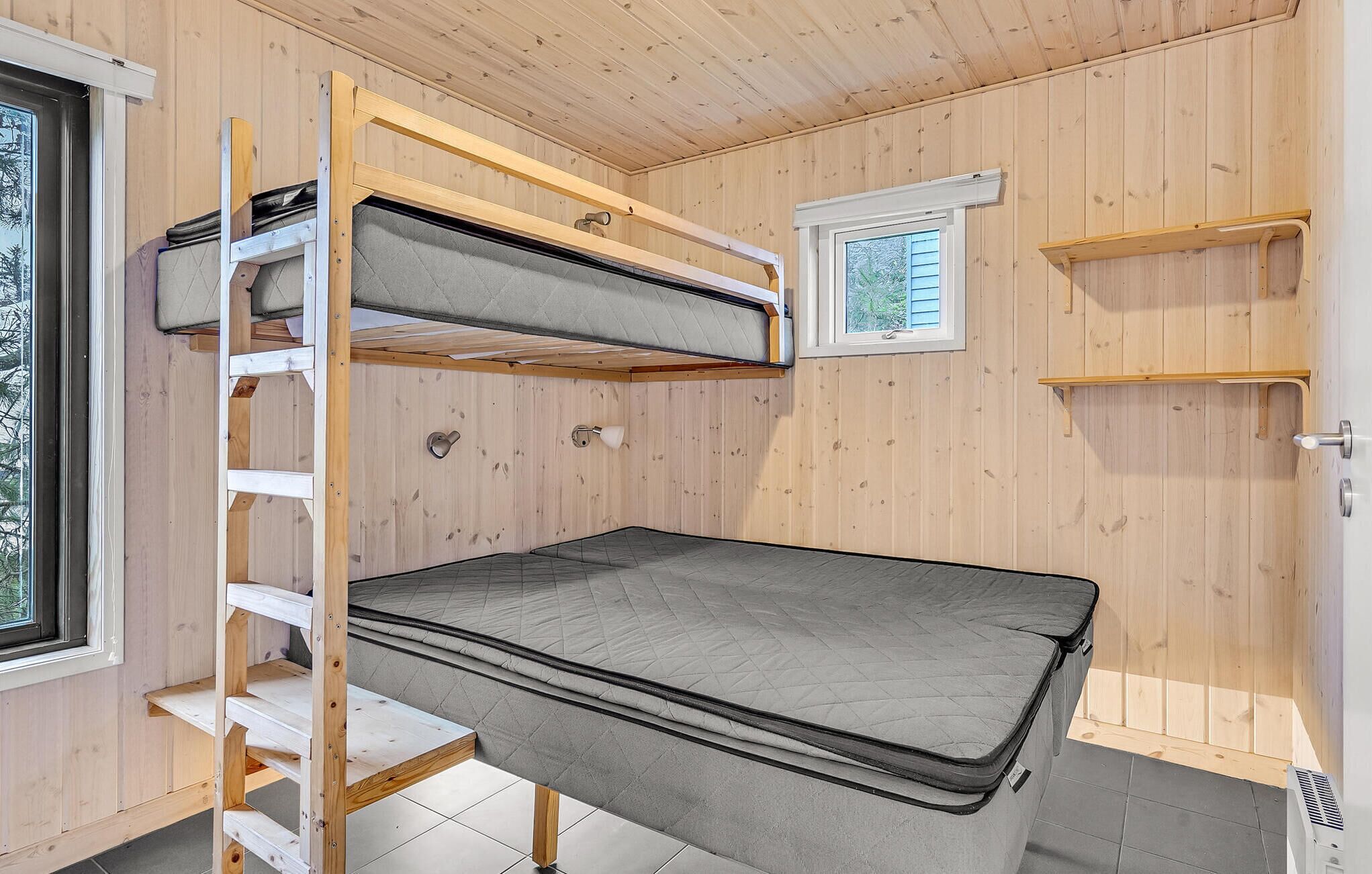 Une petite pièce avec un lit superposé, des murs en bois, une petite fenêtre et une étagère intégrée.