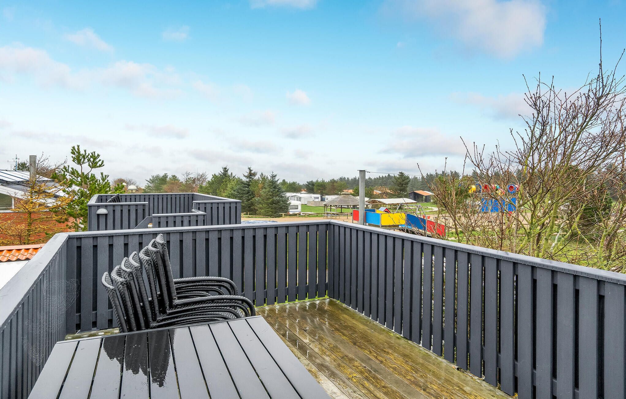 A covered outdoor area with a wooden deck and a black metal fence.