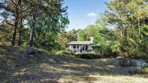 Een klein vakantiehuisje met een veranda en buiten zitplaatsen, omgeven door een dicht bos.