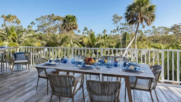 Un área de comedor al aire libre con terraza de madera, barandilla blanca y sillas de mimbre.