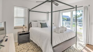 Una cama con dosel, un ventilador de techo, una mesita de noche con lámpara y vistas al exterior a través de amplias ventanas.