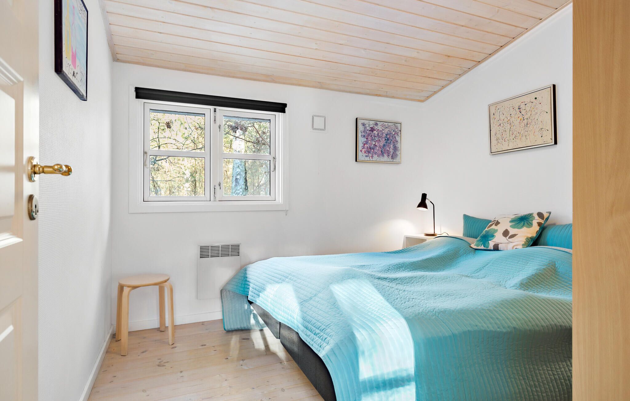 A bedroom with a bed, a window, a bedside table with a lamp, and a small stool.