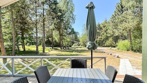 Un espacio de estar al aire libre cubierto con una mesa y sillas, rodeado de árboles y vistas a un jardín.