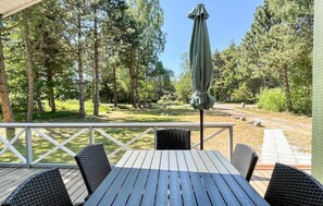 A covered outdoor seating area with a table and chairs, surrounded by trees and a view of a garden.