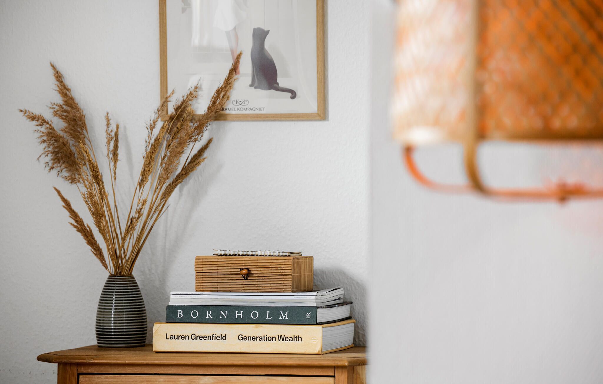 A wooden side table with a vase of dried plants, a framed picture, and a stack of books.