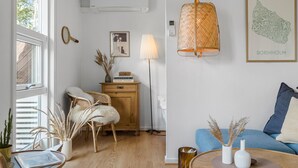 Une pièce avec un plancher en bois, une chaise en osier, un canapé bleu, un lampadaire et une carte encadrée accrochée au mur.
