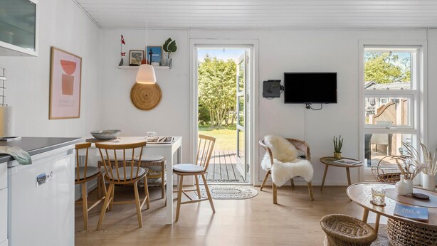 Une cuisine moderne avec des meubles en bois, un coin repas avec une chaise blanche et un téléviseur fixé au mur.
