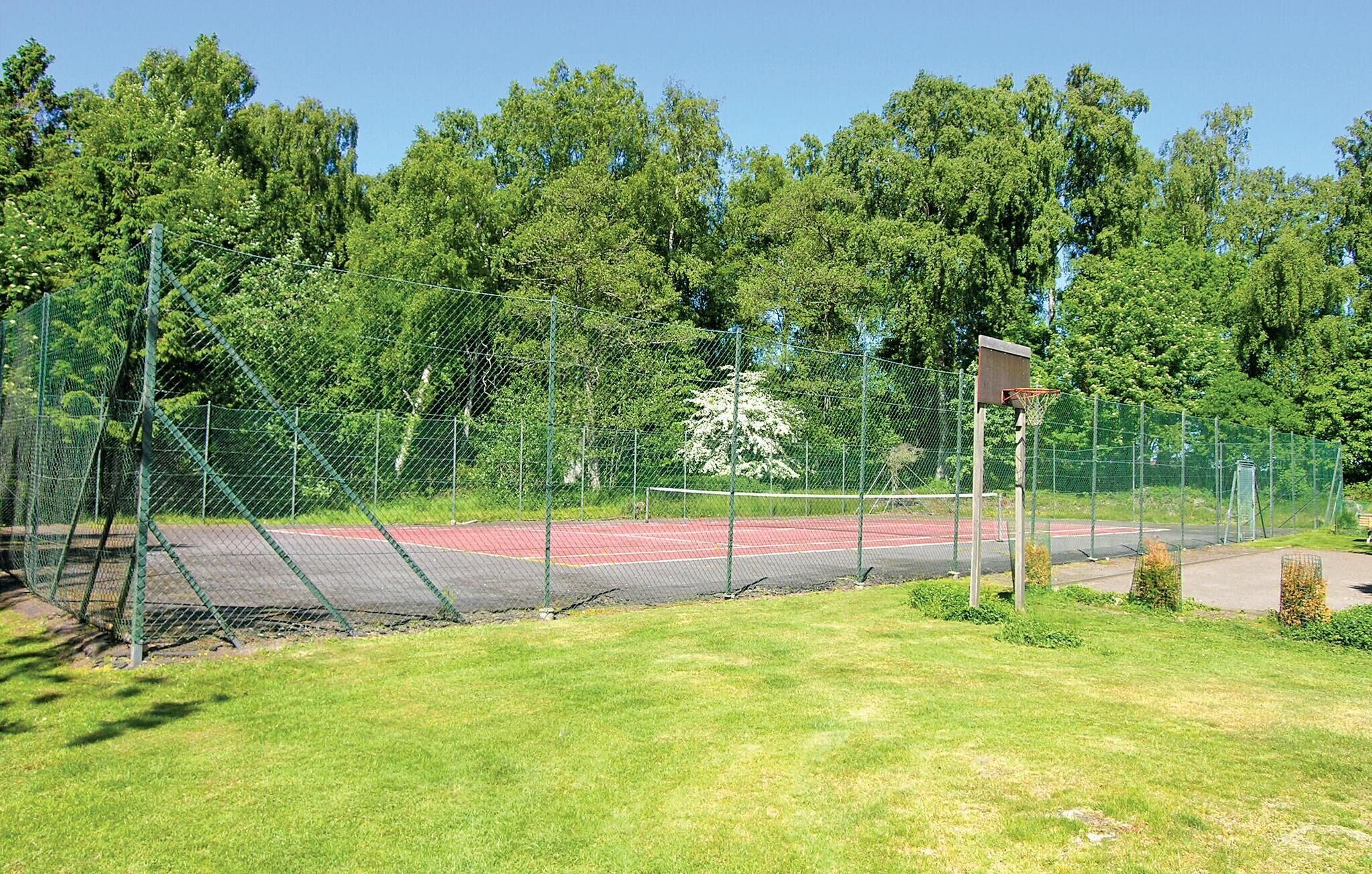 A basketball court with a red surface, surrounded by a green fence and trees.