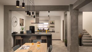 Una cocina moderna con una isla central, un comedor con mesa de madera y una escalera que sube a un nivel superior.