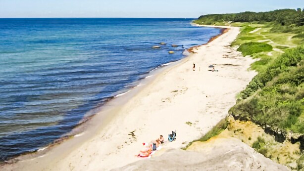 A beach with clear blue water, a sandy shore, and a few people relaxing.