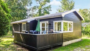 A small wooden cabin with a deck, two windows, and a green umbrella.
