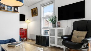 Olohuoneessa on musta nahkainen nojatuoli, puinen sohvapöytä, punainen lipasto, televisio ja ikkuna, josta avautuu näkymä taivaalle.