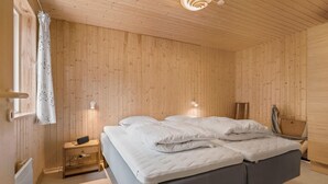 Une chambre avec un mur lambrissé en bois, un lit avec une literie blanche, une table de chevet avec une horloge et un luminaire fixé au mur.