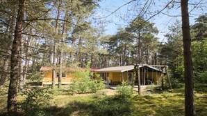 Une cabane entourée de grands pins, avec un toit rouge et une véranda.