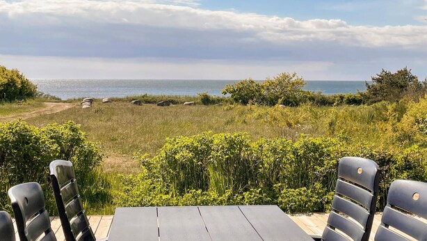 Un espace extérieur aménagé avec des sièges, offrant une vue sur la mer et entouré de verdure et de rochers.