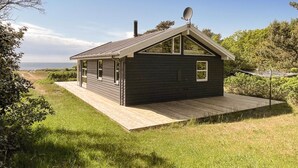 Une petite cabane de couleur sombre, dotée d’un toit en pente, d’une antenne parabolique et d’une terrasse en bois.