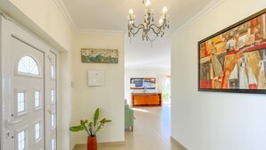 A hallway with a white door, a potted plant, a chandelier, and a painting on the wall. - Beautiful villa with ocean & lagoon views,  walk to the beach! (Vau)