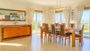 A dining area with a wooden table and chairs, a buffet counter, and large windows with curtains. - Beautiful villa with ocean & lagoon views,  walk to the beach! (Vau)