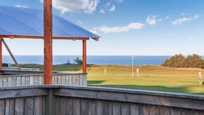 A wooden deck with a solar panel roof, overlooking a grassy area with a view of the ocean.