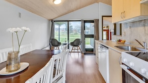A compact kitchen with a dining area, wooden ceiling, and large windows.