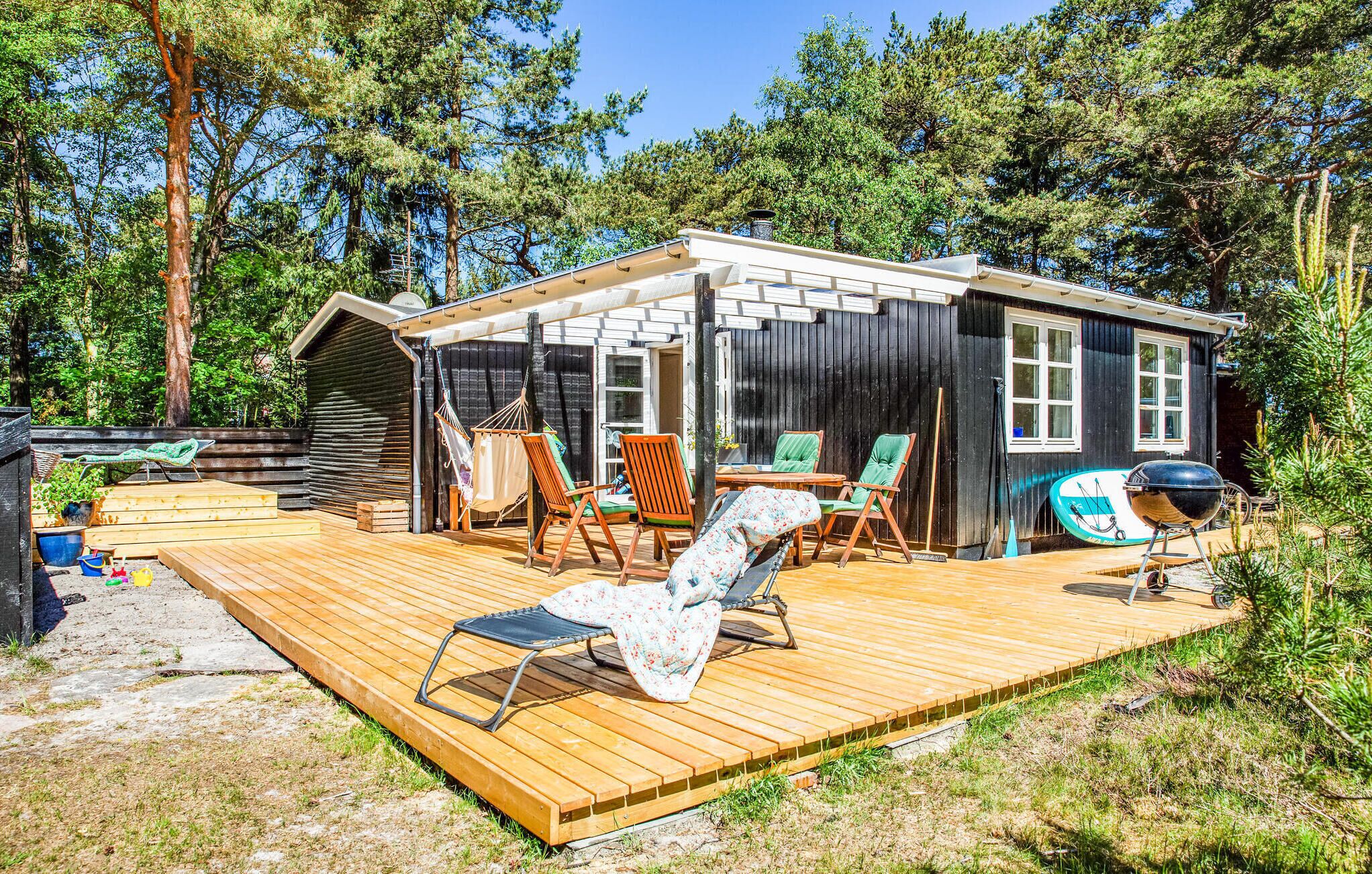 Eine Holzhütte mit einer Holzdiele, Sitzgelegenheiten im Freien und einem Grill.