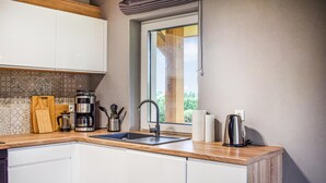 A modern kitchen with white cabinets, a wooden countertop, a coffee maker, a kettle, and a window with a view of greenery.